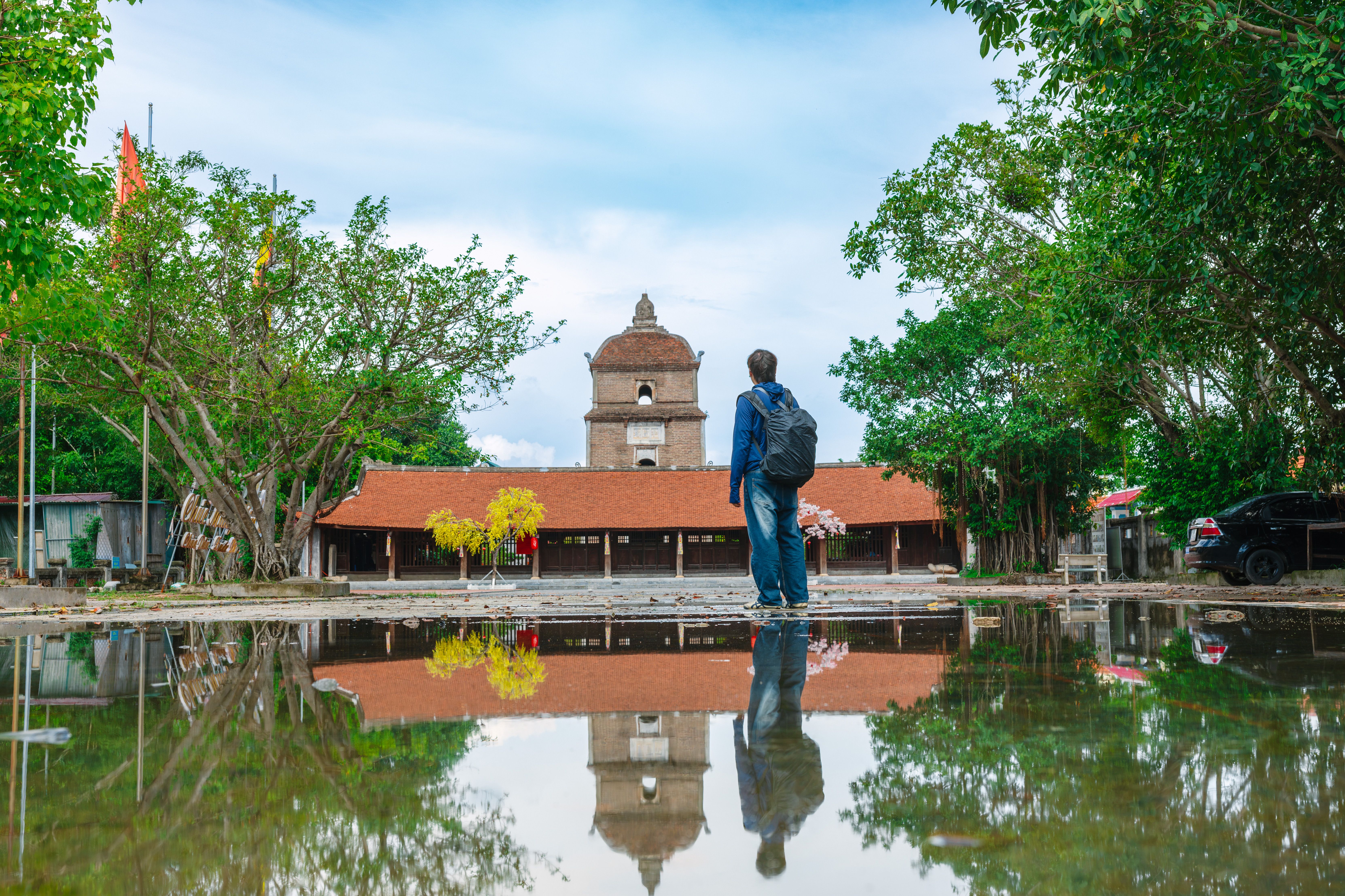 A lone traveler with a backpack standing in front of a historic temple, reflected in a calm pool.