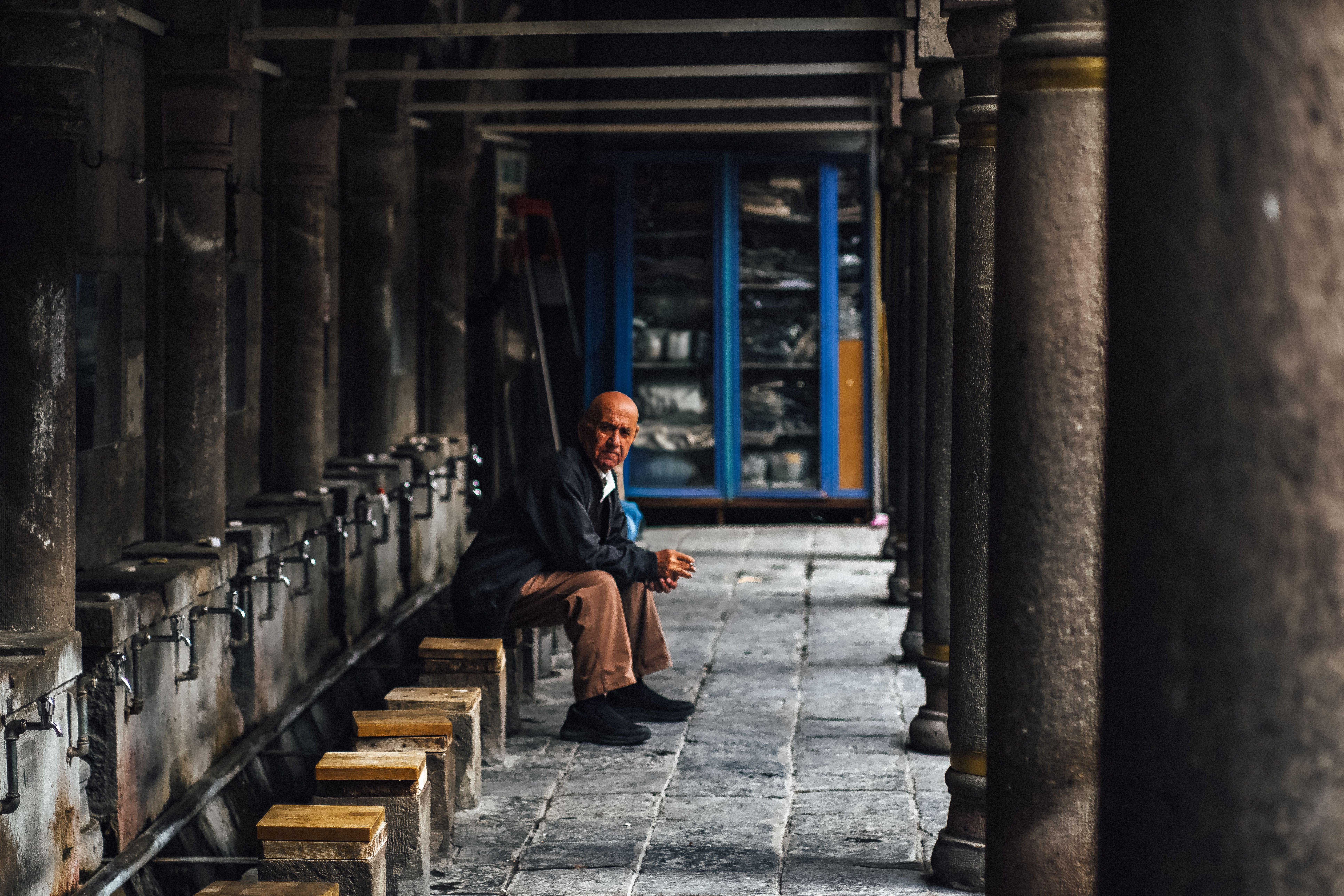 A solitary man sits in deep thought along a historic colonnade, evoking a sense of timeless reflection.
