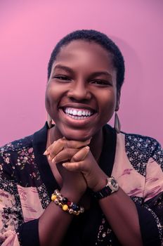 Portrait of a joyful African woman in vibrant attire with a wide smile against a pink background.