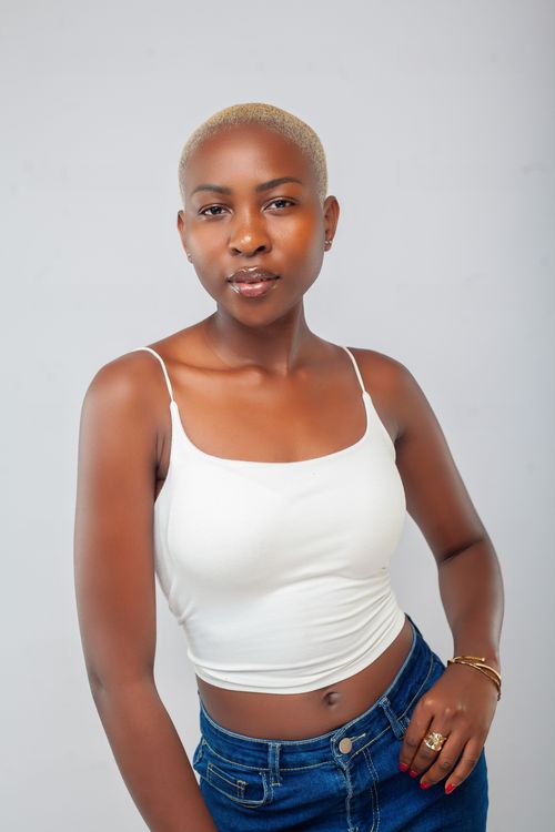 Free Portrait of a confident woman in a white tank top and jeans against a neutral background. Stock Photo