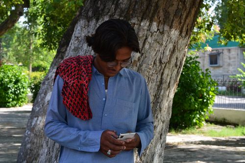 Free A young man leans against a tree, intently using his smartphone outdoors in Taxila, Pakistan. Stock Photo
