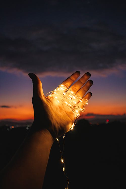 Crop unrecognizable person with garlands tied on hand against sundown sky