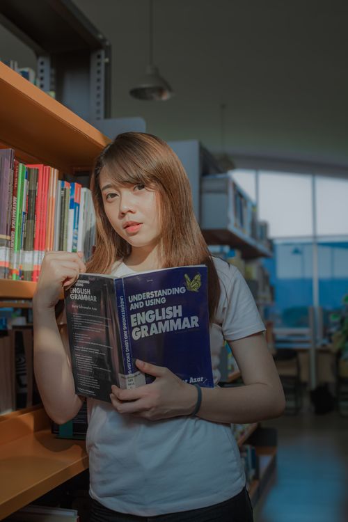 Free A young woman reads an English grammar book in a library setting. Stock Photo