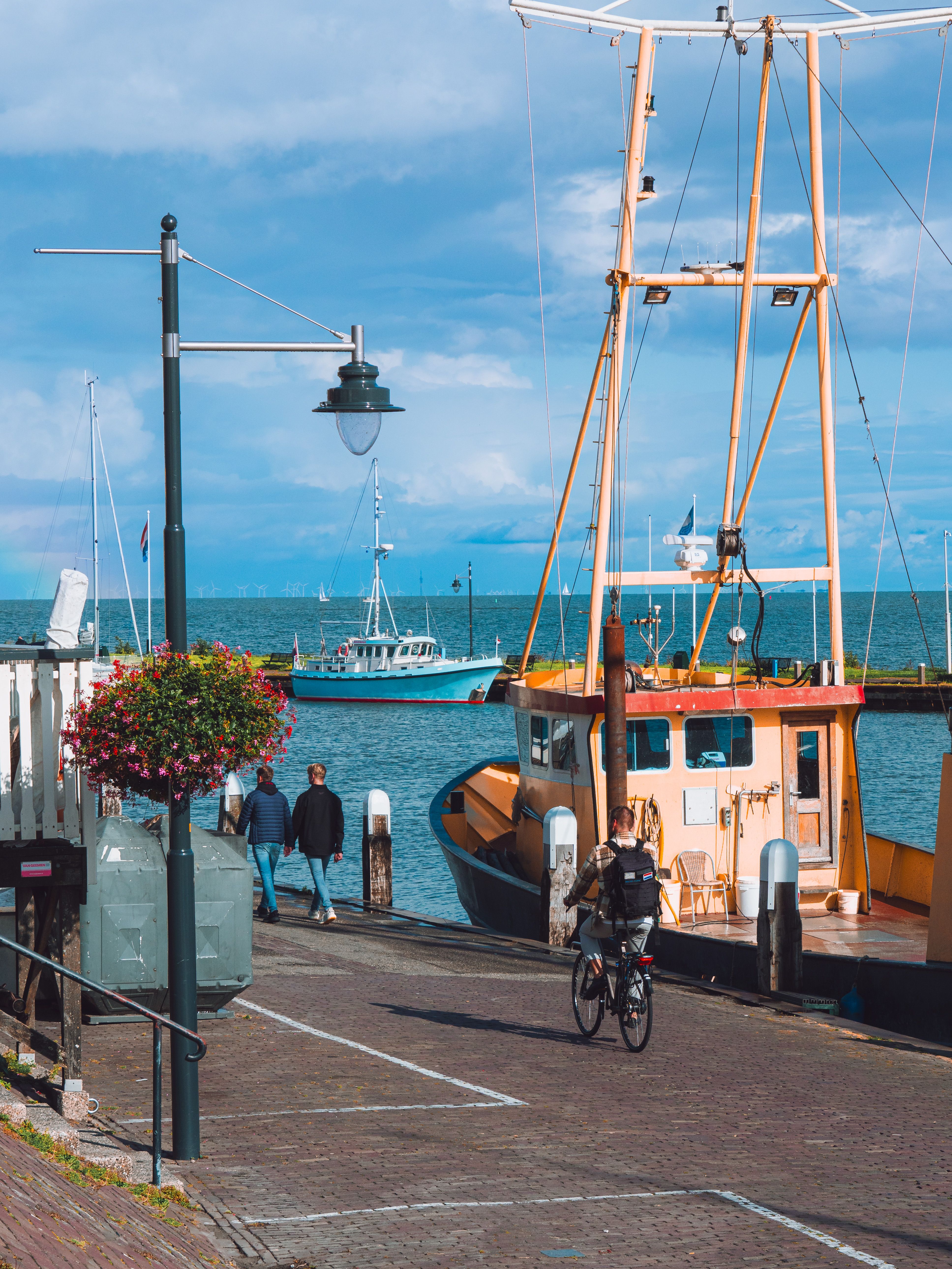 Scenic view of Volendam harbor featuring fishing boats, people, and a cyclist under a blue sky.