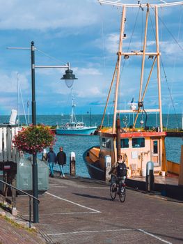 Scenic view of Volendam harbor featuring fishing boats, people, and a cyclist under a blue sky.