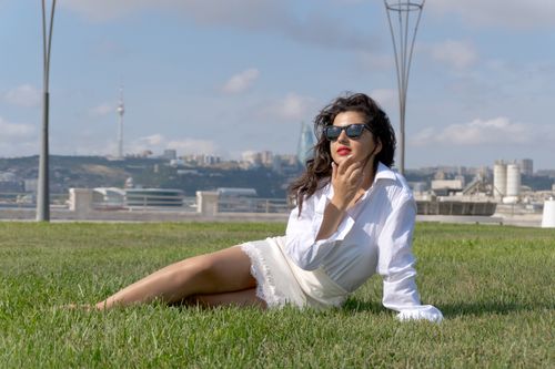 Free Stylish woman lounging on grass in Baku, with city skyline and TV Tower in the background. Stock Photo