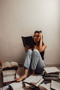 一名年轻女子坐在室内，周围散落着打开的书，正全神贯注地阅读