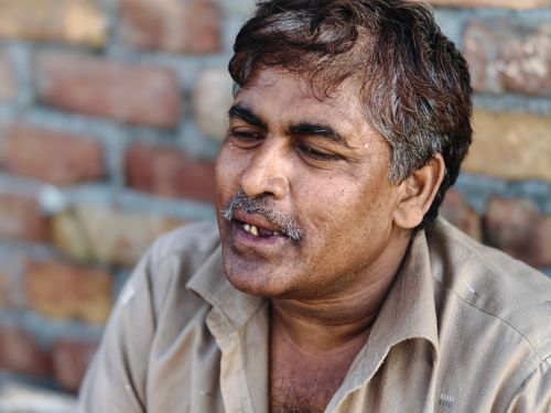 Free Casual portrait of a middle-aged man smiling against a brick wall. Warm and candid outdoor setting. Stock Photo