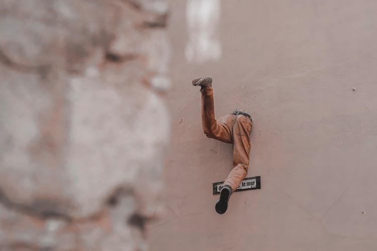 Half Body Of Unrecognizable Man Escaping Through Hole In Wall