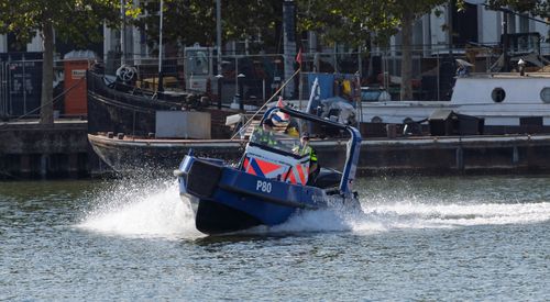 Free Police patrol boat speeding through water in an urban area with officers aboard, showcasing law enforcement at work. Stock Photo