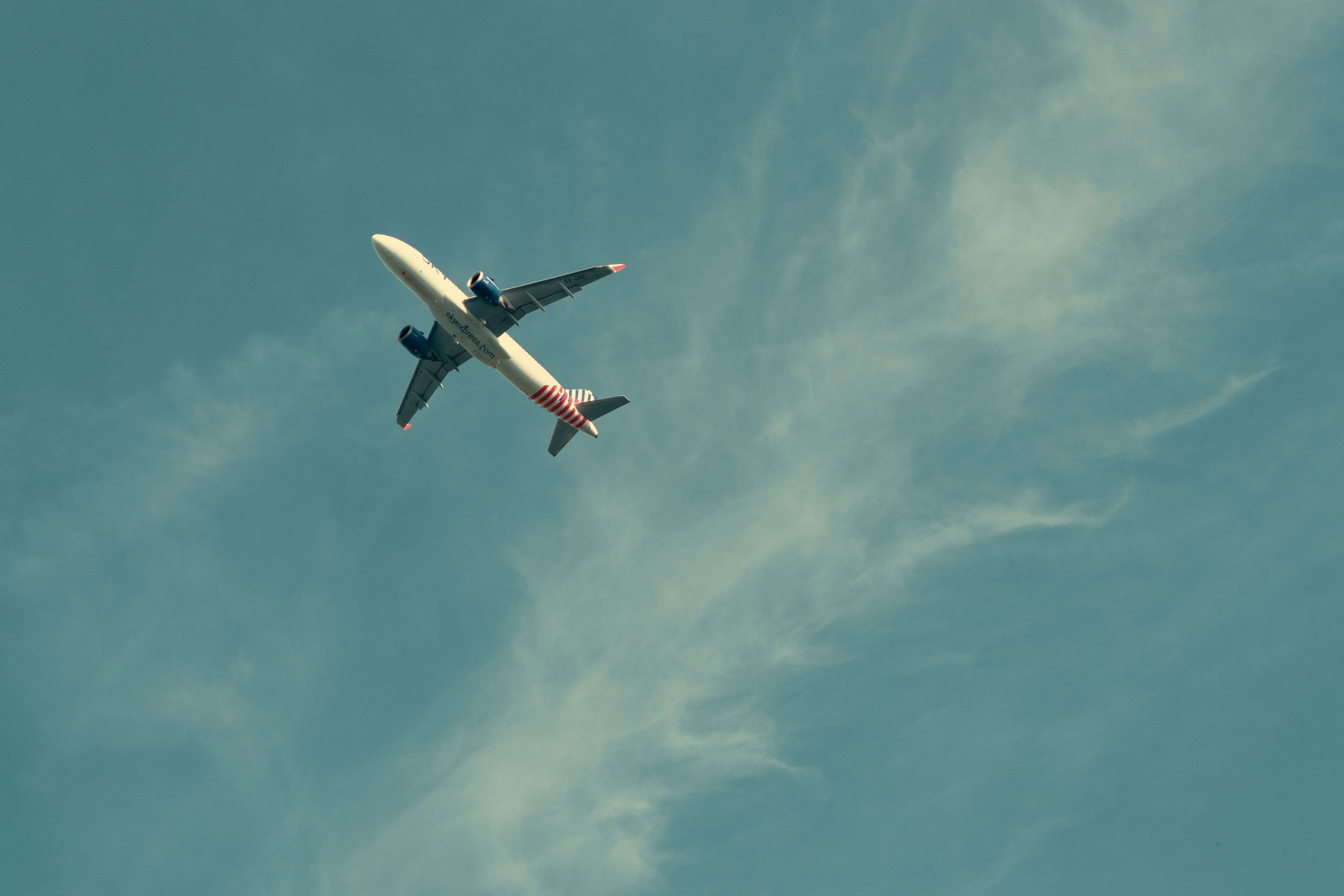 Wide shot of a jet airplane flying through a clear sky with wispy clouds.