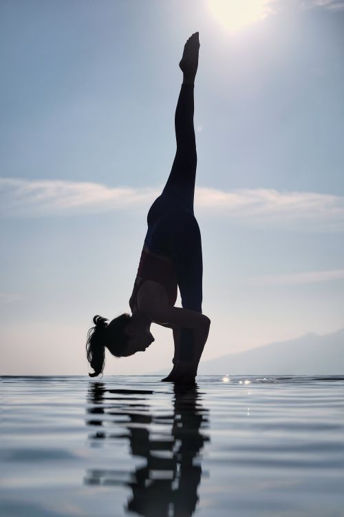 Free High-contrast silhouette of a woman performing a yoga pose by the water at sunrise in Jawa Barat, Indonesia. Stock Photo