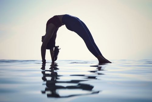 Free Silhouette of a woman practicing yoga on a reflective water surface at sunset, depicting balance and tranquility. Stock Photo
