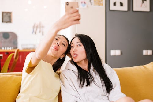 Free Woman in White Long Sleeve Shirt Sitting on Yellow Couch Stock Photo