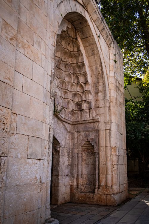 Free A historic stone archway with intricate carvings in a sunlit courtyard, surrounded by greenery. Stock Photo