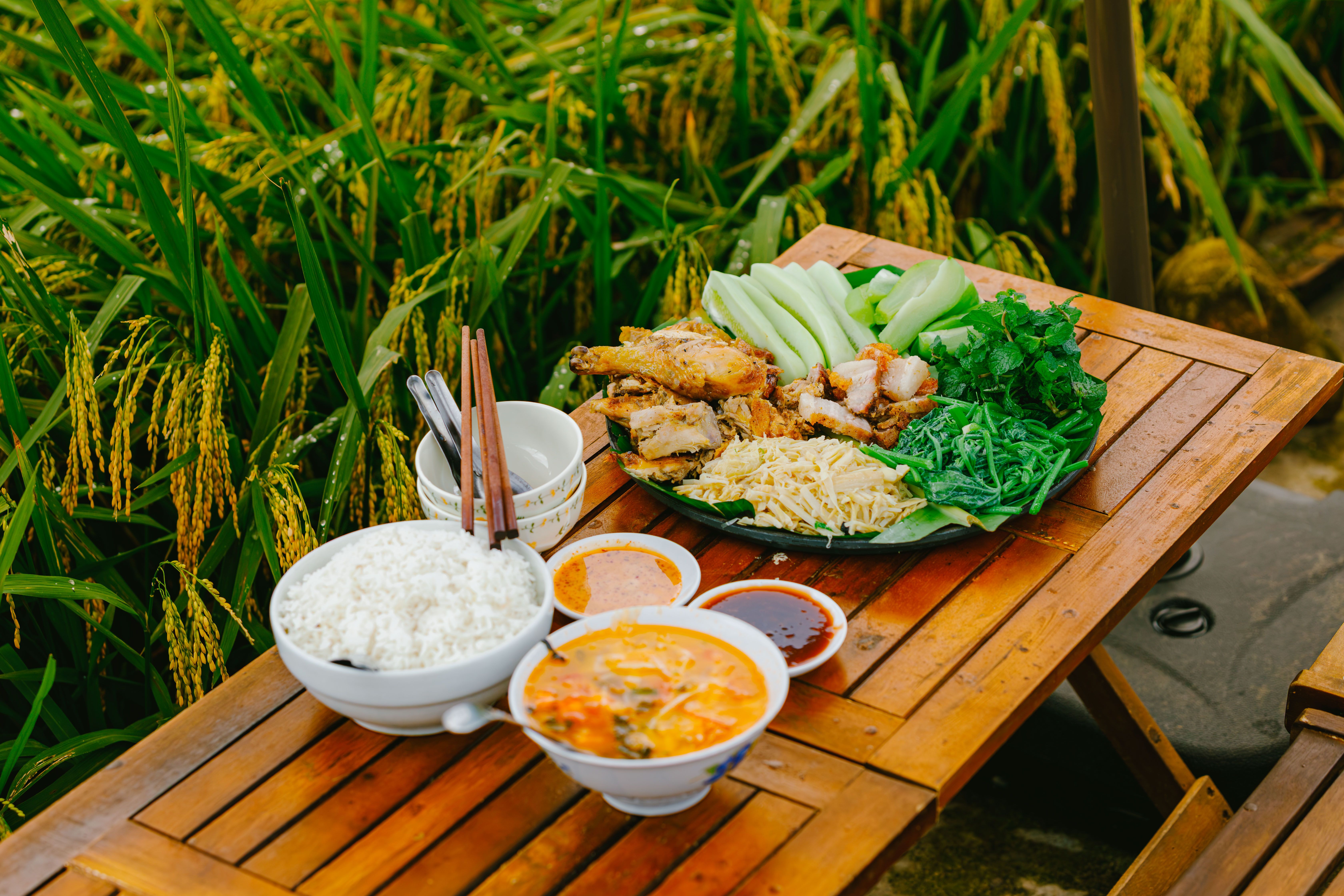 Delicious traditional Asian dishes served on a wooden table by a lush green rice field.