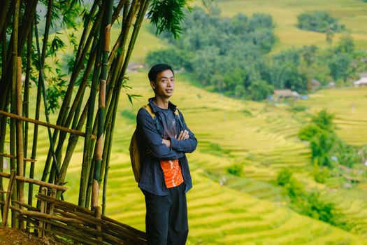 A young adult standing by bamboo, overlooking vibrant rice terraces on a bright day.