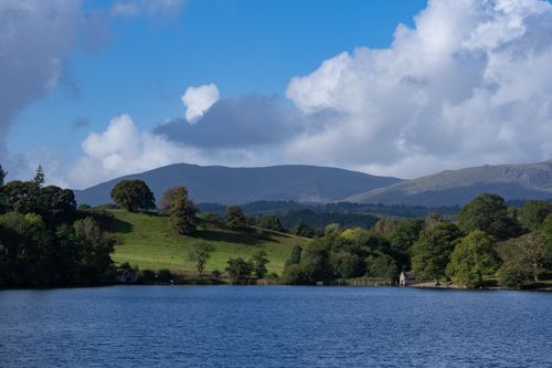 Free Beautiful lakeside view with rolling green hills and a bright blue sky in the background. Stock Photo