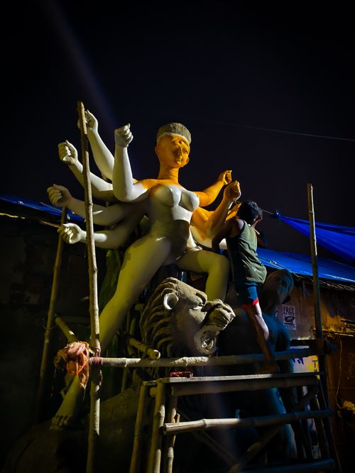 Free An artist intricately sculpts a giant Hindu goddess statue during nighttime, under compelling lighting. Stock Photo