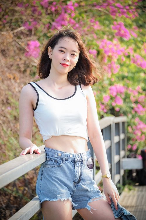 Free Asian woman in casual attire smiling in front of vibrant pink flowers outdoors, Vietnam. Stock Photo