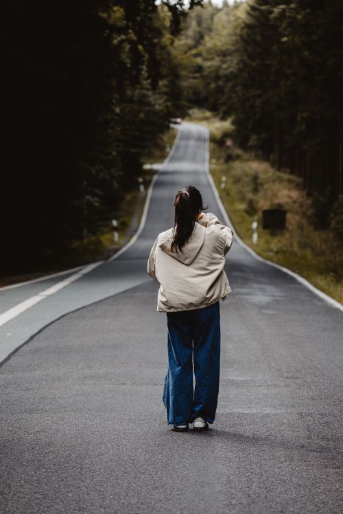 Free A woman walks down a quiet forest road in Großschönau, Saxony, Germany, surrounded by lush greenery. Stock Photo