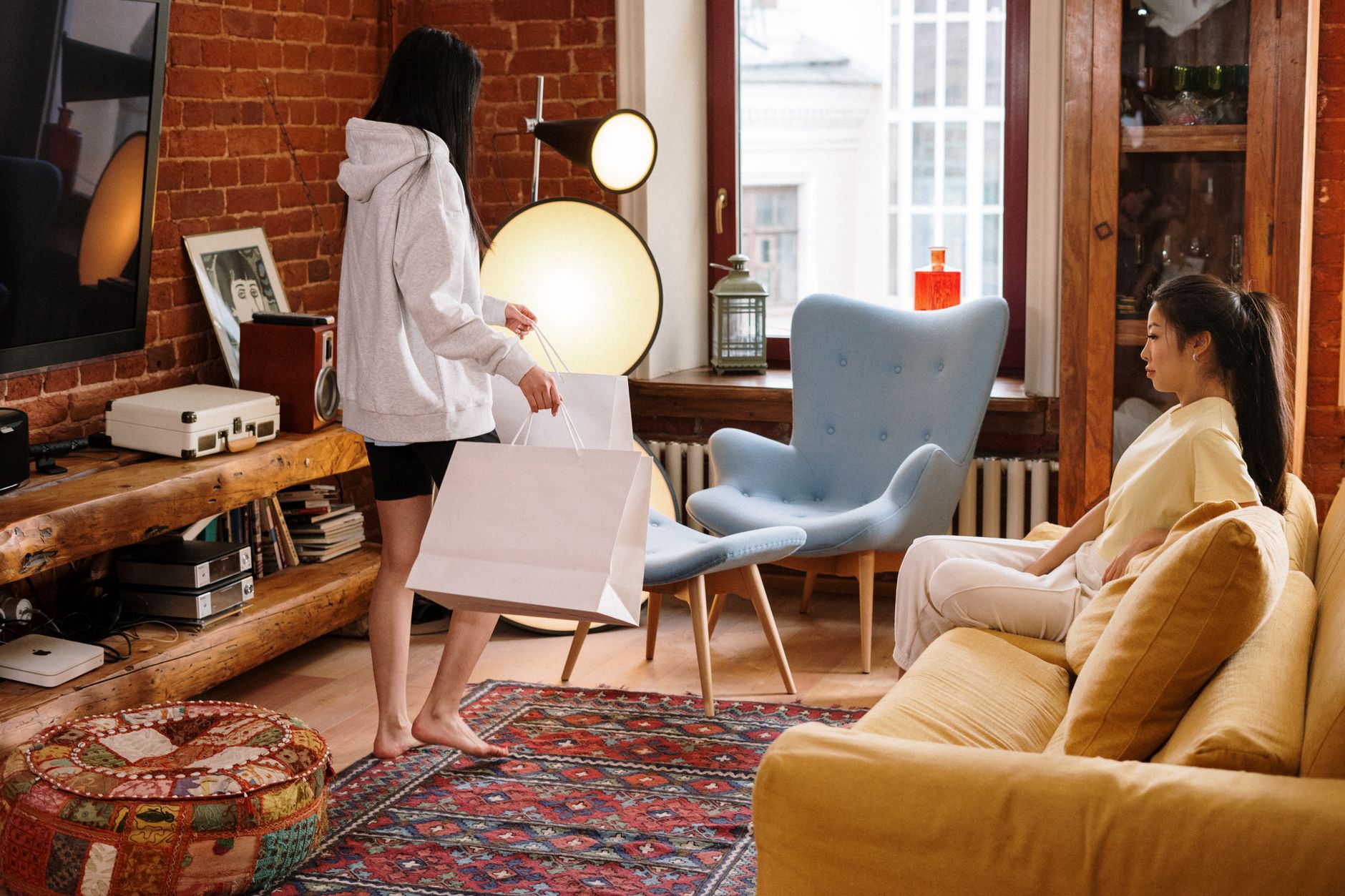 Two friends enjoying a relaxing time in a stylish living room with shopping bags and a cozy atmosphere.