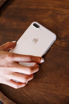 Close-up of a hand with manicured nails holding a smartphone on a wooden surface.