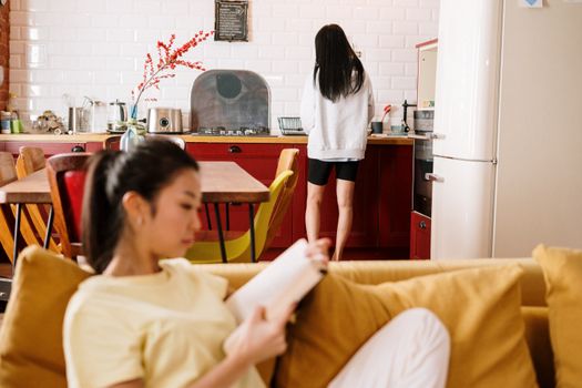 两个女人在家放松，一个在沙发上读书，另一个在厨房柜台前读书