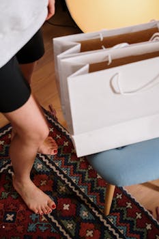 A woman stands barefoot at home with shopping bags, highlighting coziness and online shopping lifestyle.