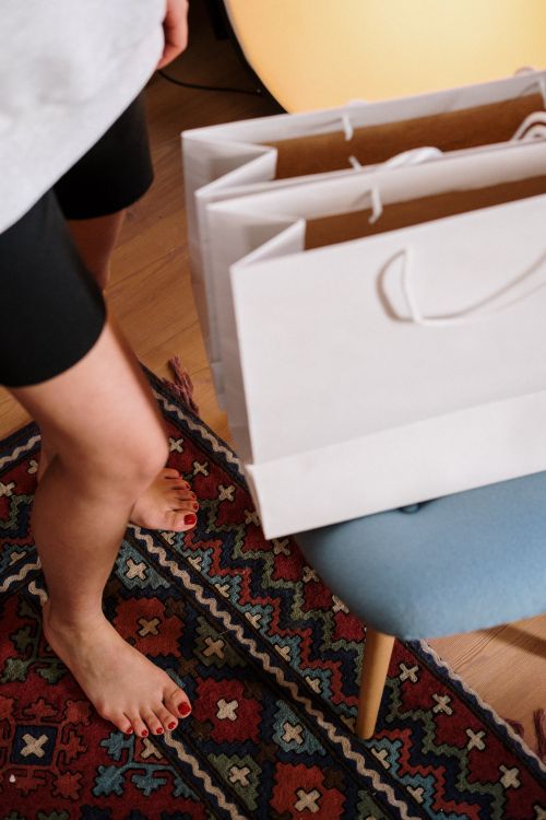 Free A woman stands barefoot at home with shopping bags, highlighting coziness and online shopping lifestyle. Stock Photo