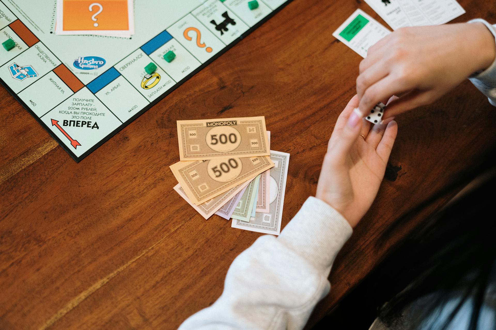 Hands holding dice near Monopoly board with fake money on table.