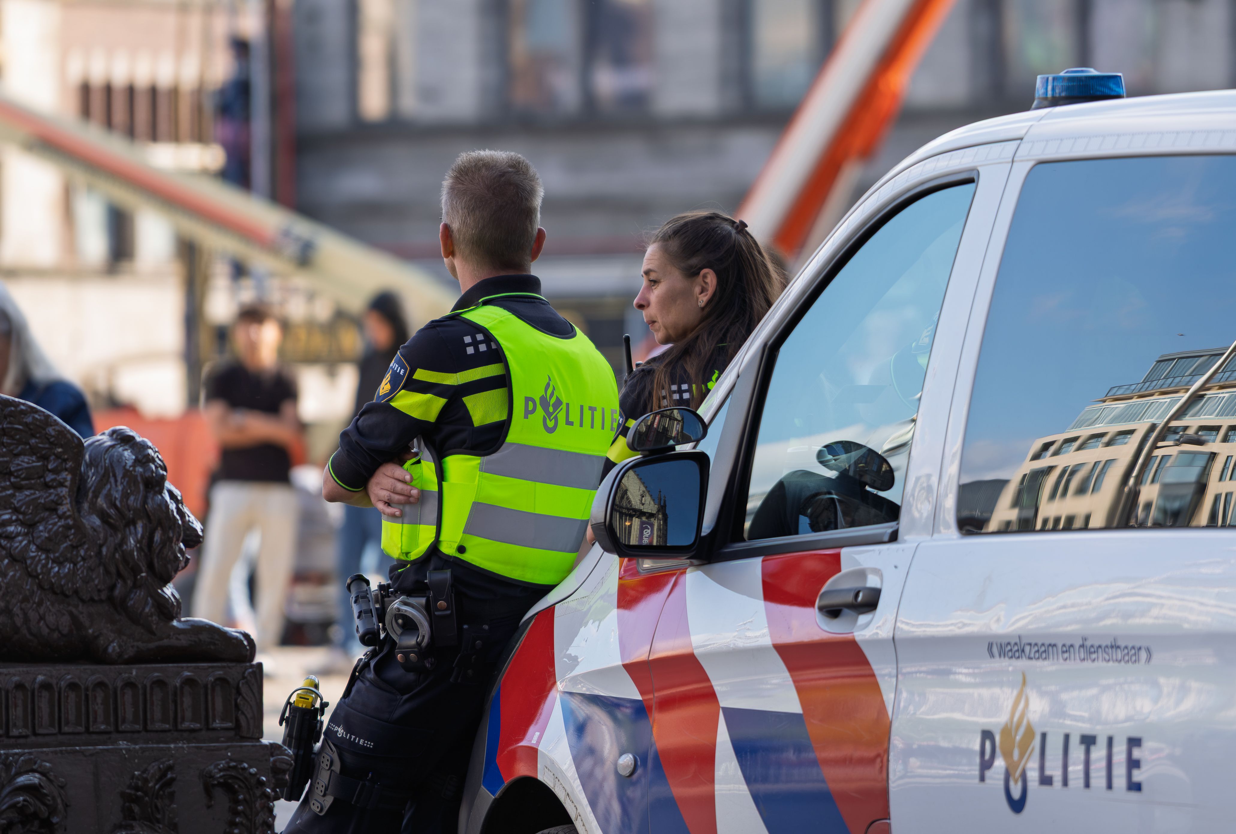 Twee politieagenten staan ​​naast een herkenbare patrouillewagen in een stedelijke omgeving en zorgen voor de beveiliging.