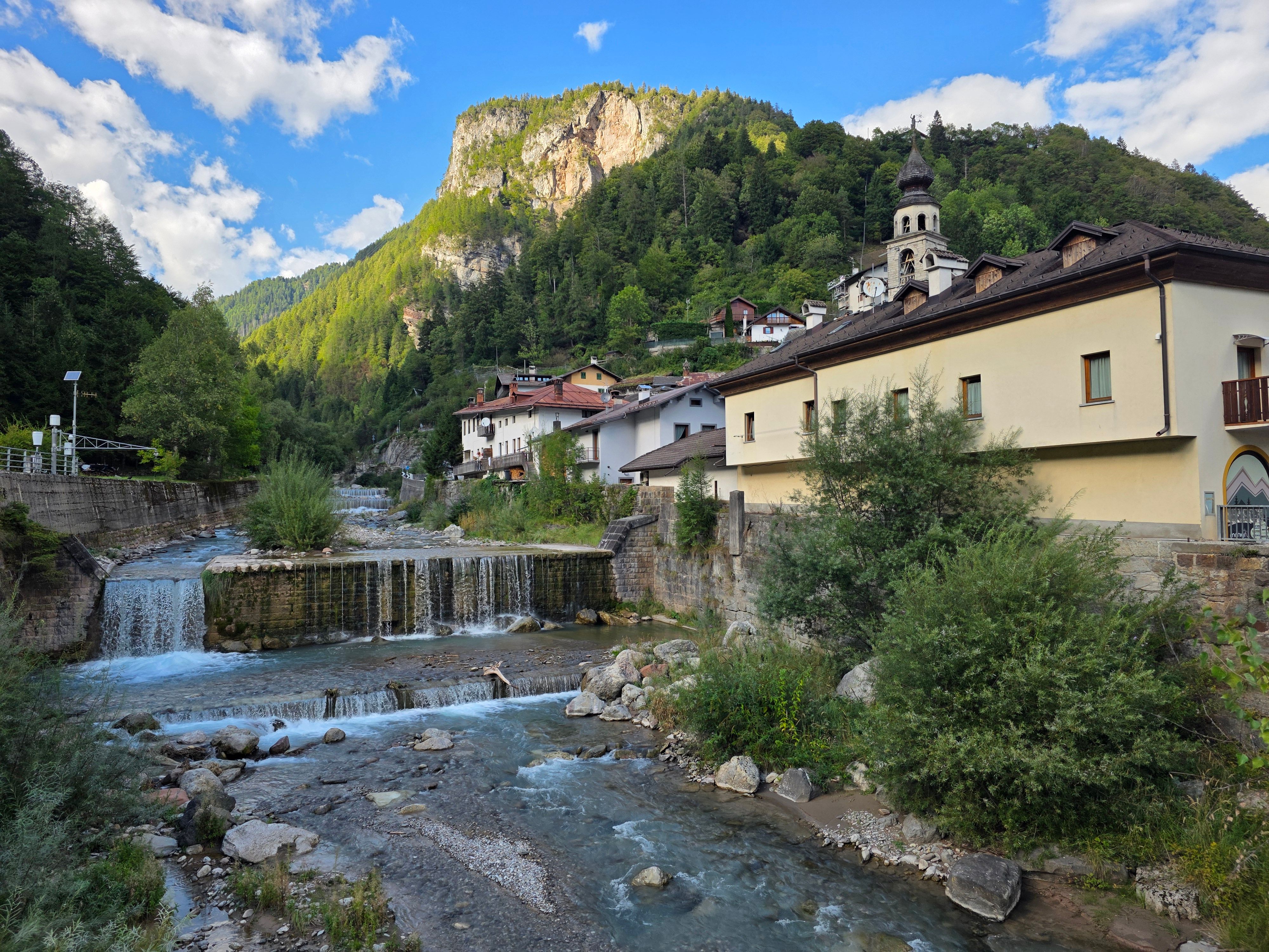 Picturesque mountain village with a flowing river and church under a clear blue sky.