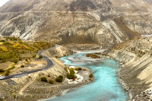 Free Scenic view of a winding mountain road alongside a turquoise river in a rocky landscape. Stock Photo