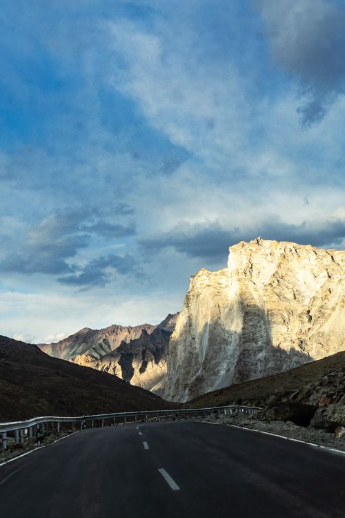 Free Beautiful mountain road leading to spectacular peaks under a dramatic sunset sky. Stock Photo