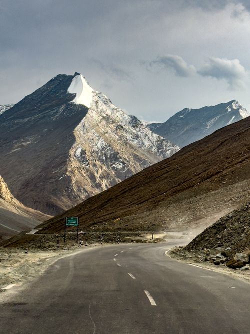 Free A winding road leads into remote, snow-capped mountains under a cloudy sky, highlighting adventure and solitude. Stock Photo