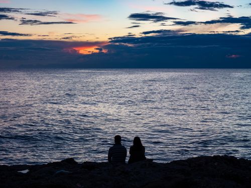 Free Silhouette of a couple watching a stunning sunset over a calm sea, creating a romantic mood. Stock Photo
