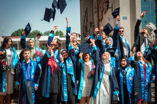 Free Joyful graduates toss caps in the air after ceremony, celebrating outdoors on a sunny day. Stock Photo