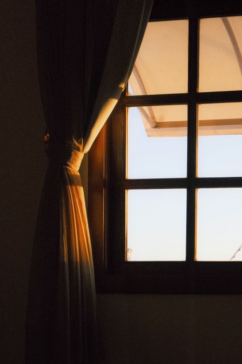 Free Cozy interior with warm sunlight streaming through a curtained window, creating a serene ambiance. Stock Photo