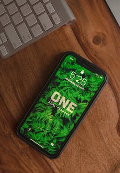Smartphone displaying a nature-themed wallpaper on a wooden desk beside a keyboard.