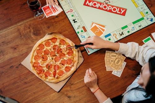Pizza and Monopoly Board Game on Wooden Surface 