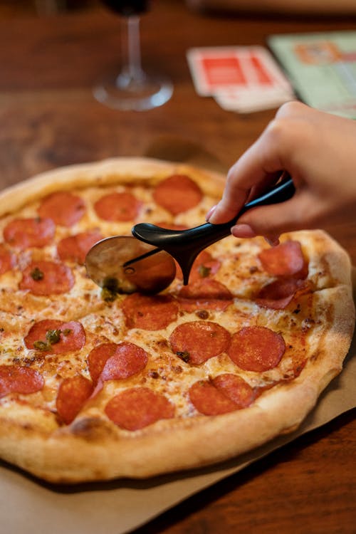 Free Person Slicing Pizza on Brown Wooden Table Stock Photo