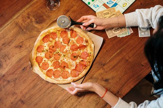 Top view of a pepperoni pizza and board game setup on a wooden table, perfect for a cozy night in.
