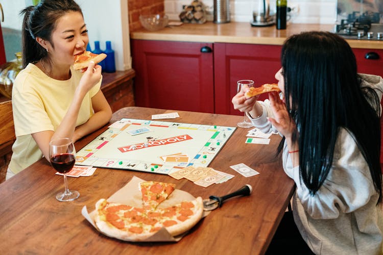 Women Snacking On Pizza While Playing Monopoly 