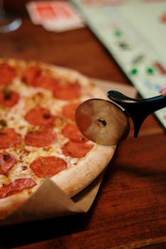 Close-up of a pepperoni pizza being sliced with a pizza cutter indoors on a wooden table.