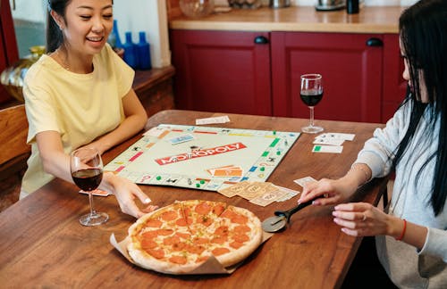 Free Women Snacking on Pizza while Playing Monopoly  Stock Photo