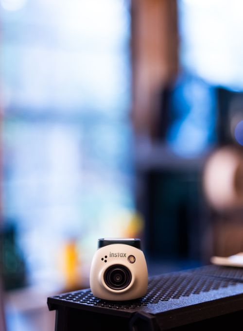 Free Modern Instax camera on table with a soft focus background, creating a nostalgic and artistic feel. Stock Photo