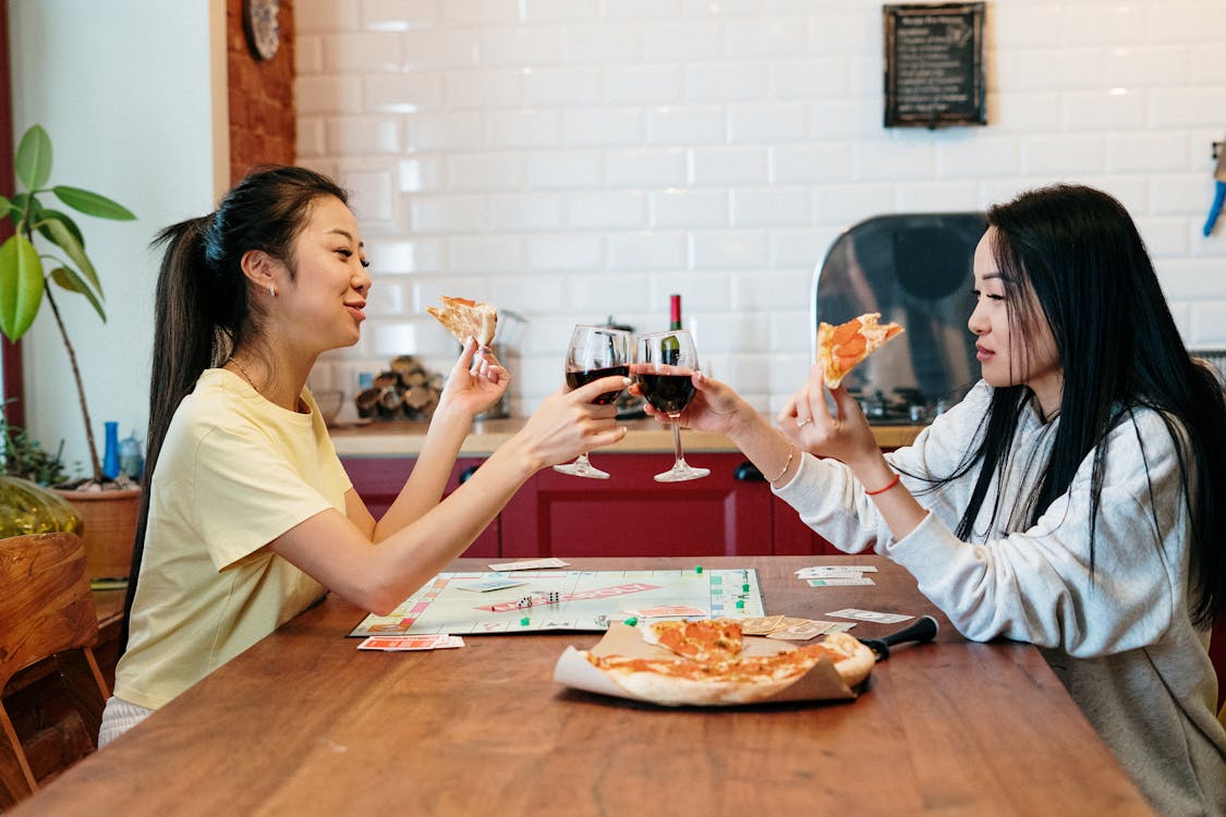 Woman in White Shirt Holding Wine Glass Sitting Beside Brown Wooden Table