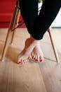 Person With Red Pedicure Standing on Brown Wooden Floor
