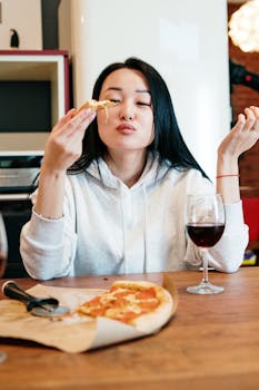Woman savoring a pizza slice with a glass of wine in a cozy home setting.